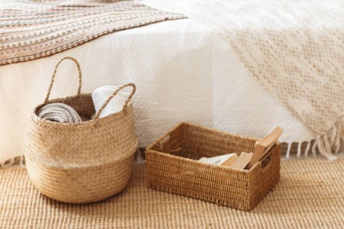 folded gray knitted plaid in straw basket on wicker carpet near bed. cozy hygge home style. fall winter season concept. close up, copy space. - home decoration stockfoto's en -beelden