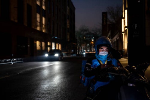 Food delivery driver waits for take-out orders on a quiet street at a shopping mall and restaurant area where inside dining is prohibited and shops...