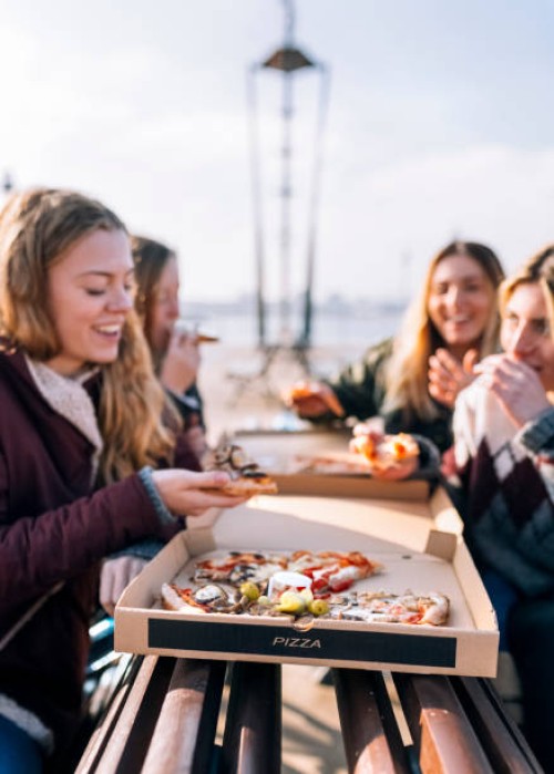 four friends eating pizza outdoors - junk food stock pictures, royalty-free photos & images