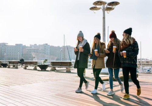 four friends with coffee to go and cell phones walking on promenade in winter - junk food stock pictures, royalty-free photos & images