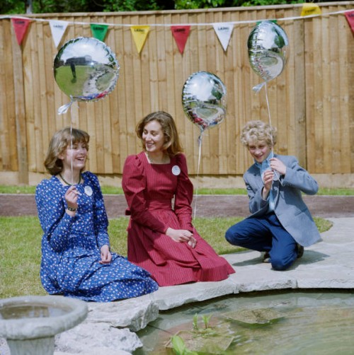Four Limes, Wheathampstead, St. Albans, Hertfordshire, . Three young people with balloons kneeling beside the pond in the communal garden at the Four...