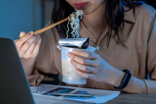 freelance women eating instant noodles while working on laptop in living room at home at night. - junk food stock pictures, royalty-free photos & images