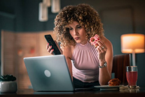 freelancer woman eating breakfast while working at laptop from home - junk food stock pictures, royalty-free photos & images