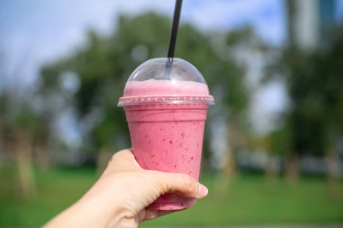 fruit smoothy in plastic take away cup in a woman's hand over city and park background - junk food stock pictures, royalty-free photos & images