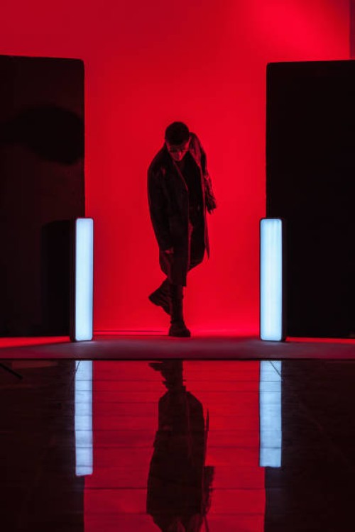 full length of young man standing amidst illuminated lights with reflection on floor in red studio - fashion stock-fotos und bilder