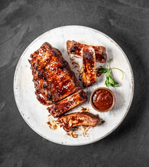 full rack of grilled barbecue ribs with barbecue sauce on cutting board on black background - food stock pictures, royalty-free photos & images