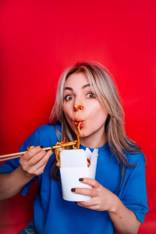 funny woman smeared in sauce sucking noodles from box using chopsticks and look at camera - junk food stock pictures, royalty-free photos & images