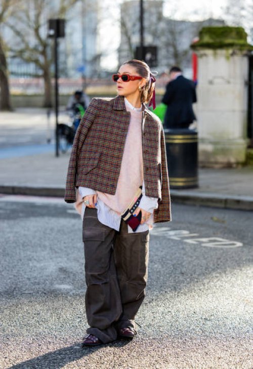 Gabby Martin wears red Prada sunglasses, checkered jacket, oversized knit, grey pants with side pockets outside Holzweiler during London Fashion Week...