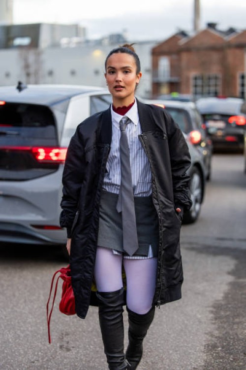 Gabriela Sevillano Fernández wears black bomber coat, red bag, over knees boots, grey tie, button shirt outside Mfpen during the Copenhagen Fashion...