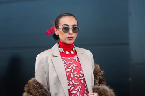 Gabriella Berdugo wears sunglasses, a bejeweled necklace , a red turtleneck pullover with white floral print , a brown fluffy faux fur coat, a beige...