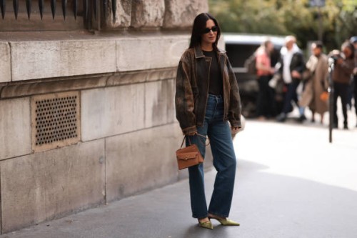 Gala Gonzalez is seen wearing oval black sunglasses from Gucci, an oversized distressed brown leather jacket, a dark brown top with high round...
