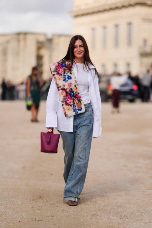 Gala Gonzalez wears white button up long sleeve shirt, navy blue denim jean pants, dark brown leather boots, dark red leather bag, outside Loewe,...