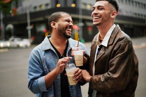 gay friends drinking ice coffee and laughing on a sidewalk in the city - coffee stock pictures, royalty-free photos & images