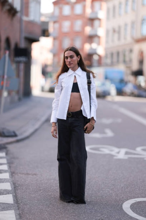 George Gorg is seen wearing golden hoop earrings; a white, long-sleeved shirt with a wide collar that is only buttoned at the top; underneath a black...