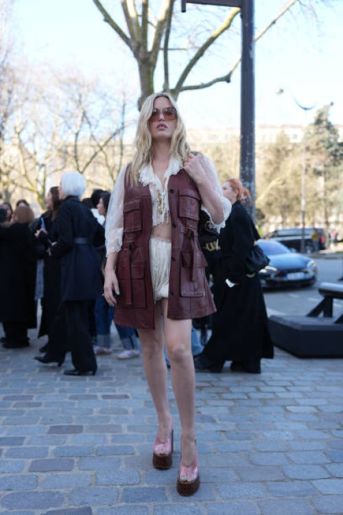 Georgia May Jagger wears dark brown sunglasses, white lace cropped sheer mesh Chloe top, shiny burgundy bordeaux Chloe leather vest, white mini...