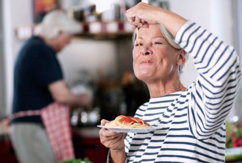 germany, wakendorf, senior woman eating noodles, man cooking in background - food stock pictures, royalty-free photos & images