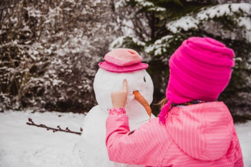 girl dressed in winter clothes makes a snowman in the backyard of their house in winter - garden decoration stock pictures, royalty-free photos & images