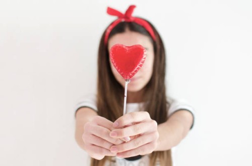 girl holding a heart shaped lollipop in front of her face - junk food stock-fotos und bilder