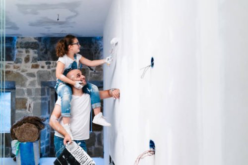 girl sitting on father's shoulders painting the wall of her new house - home decoration stock pictures, royalty-free photos & images