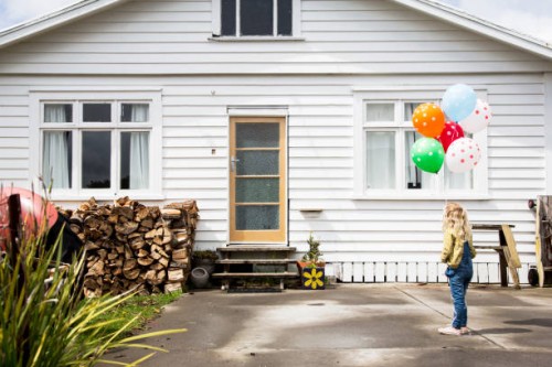 girl stands in front of a bungalow holding colourful balloons - garden decoration stock pictures, royalty-free photos & images