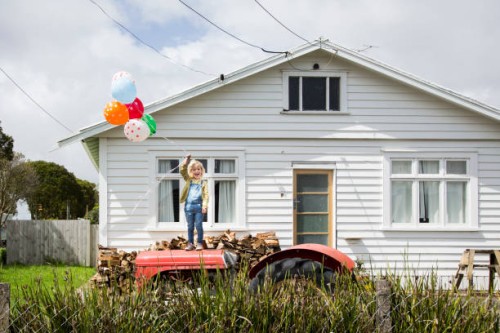 girl stands on a tractor holding colourful balloons in front of a bungalow - garden decoration stock pictures, royalty-free photos & images
