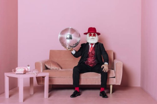 glamorous santa claus with disco ball sitting on sofa in pink room. concept fashion christmas party. - fashion stock pictures, royalty-free photos & images
