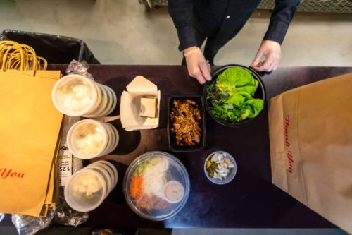 gloved man putting boxes of food in bags for delivery during covid-19 pandemic - junk food stock pictures, royalty-free photos & images