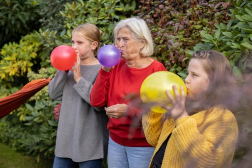 grandmother and granddaughters blowing up balloons in garden together - garden decoration stock pictures, royalty-free photos & images