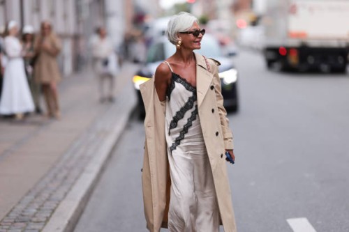 Grece Ghanem is seen wearing large gold hoop earrings; oval sunglasses with a tortoiseshell frame from Prada; a beige trench coat; underneath a...