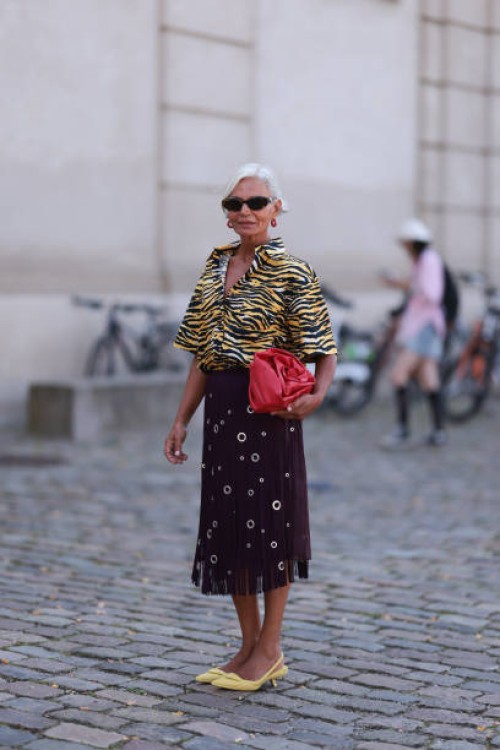 Grece Ghanem is seen wearing oval tortoiseshell sunglasses from Prada, red hoop earrings with a white dot pattern, a shirt with wide sleeves in a...
