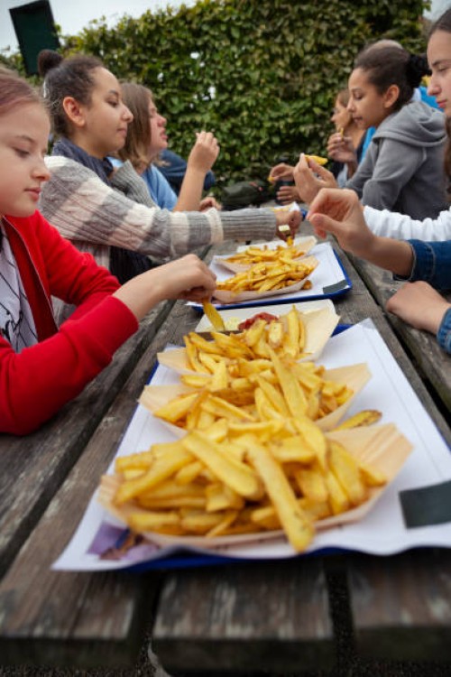 group of people sitting at an outdoor picnic table eating takeaway fast food chips - junk food stock pictures, royalty-free photos & images