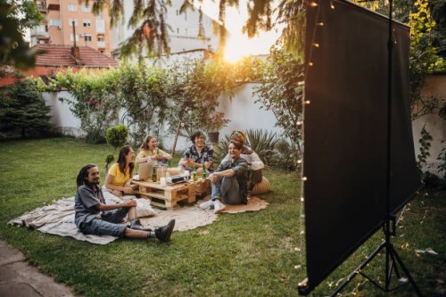 groupe d’amis se réunissant, regardant un film sur projecteur dans le jardin et traînant - garden decoration photos et images de collection
