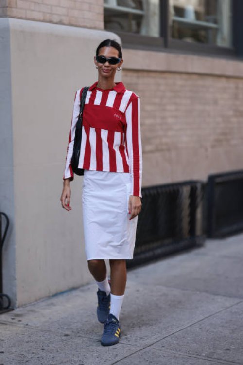 Guest is seen outside Brandon Maxwell show wearing blue sunnies, silver hoop earrings, white and red striped shirt, white midi cargo skirt and blue...