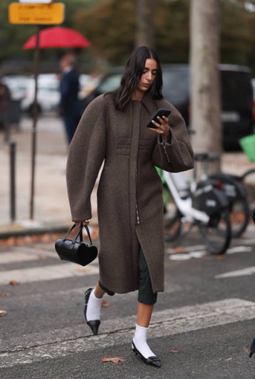 Guest is seen outside Chanel show wearing brown oversized round shaped coat, black leather handbag, white socks and black ballet flats during the...
