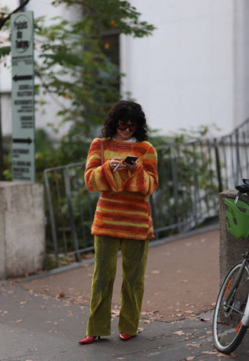 Guest is seen Outside Peter Do show wearing orange colored Loewe sunnies, red, orange and yellow colored knit sweater, green velvet pants and red...