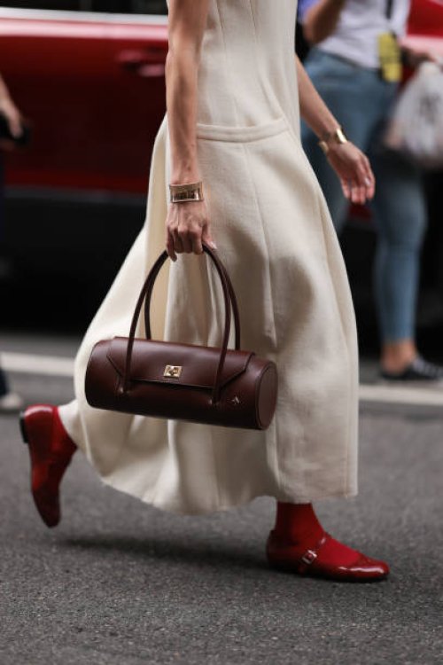 Guest is seen outside Tibi show wearing beige colored cotton dress with free arms, golden chunky bracelet, brown round shaped handbag woith golden...