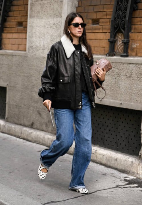 Guest is seen wearing a black and faux fur collar bomber jacket, blue jeans and white and black shoes with tan bag outside the Lacoste show during...