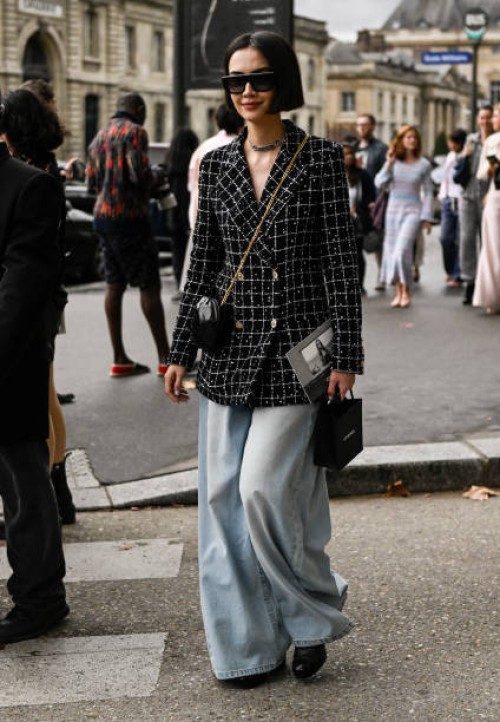 Guest is seen wearing a black and white tweed Chanel jacket, black and gold chain bag, light blue oversized jeans and black sunglasses outside the...