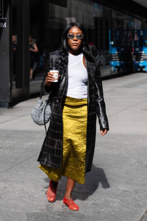 Guest is seen wearing a black coat, white top, green skirt, red mesh shoes, silver sunglasses and carrying a silver bag outside the Carolina Herrera...