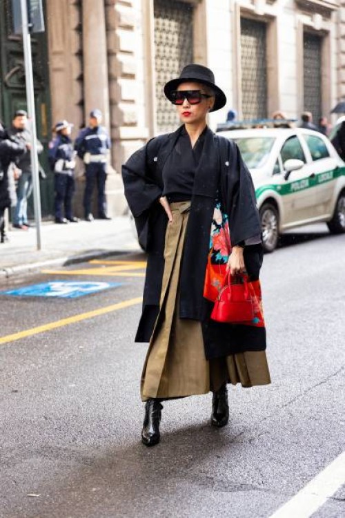 Guest is seen wearing a black hat, black and red sunglasses, a black shirt, a black and flower printed scarf, a red leather bag, a khaki long skirt...