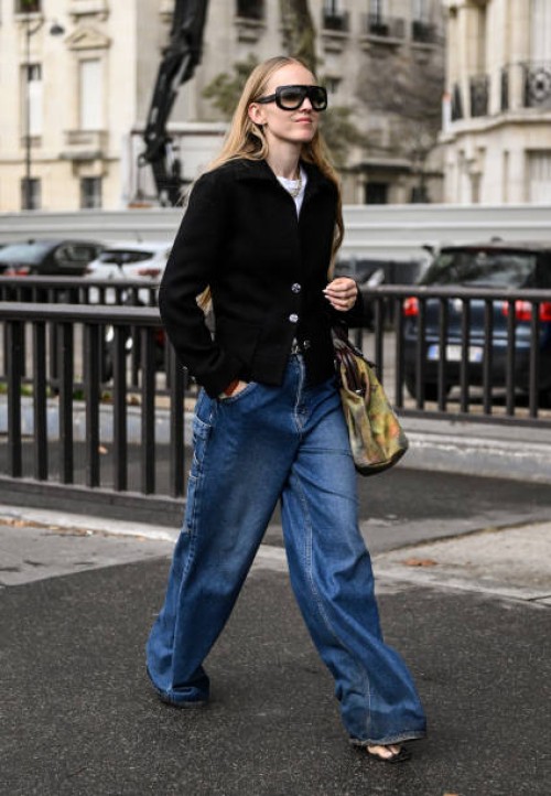 Guest is seen wearing a black jacket, white shirt, blue jeans and green bag with black sunglasses outside the Chanel show during the Womenswear...
