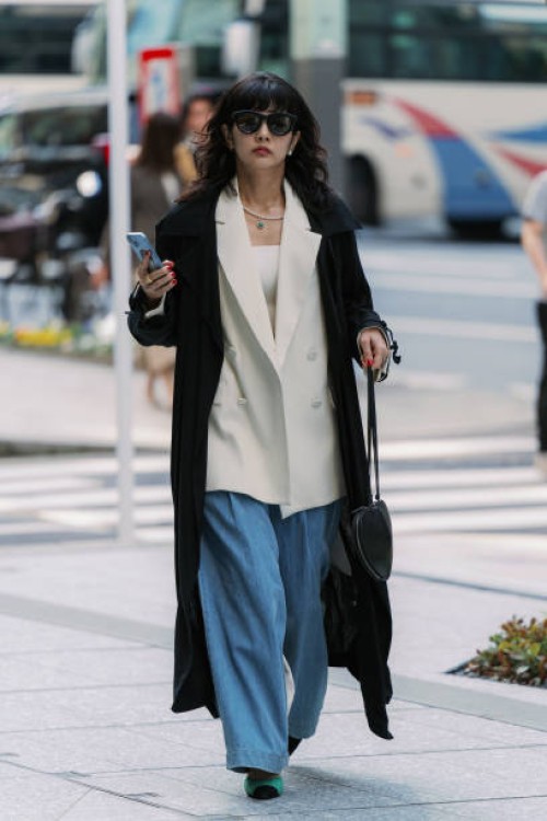 Guest is seen wearing a black trench coat, beige jacket, jeans, ALAÏA handbag, green shoes during Rakuten Tokyo Fashion Week A/W 2025 on March 22,...