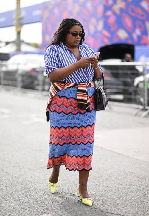Guest is seen wearing a blue and white stripe shirt, red and blue skirt and lime green shoes with black sunglasses and a black bag outside the Dior...