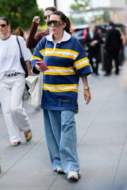 Guest is seen wearing a blue and yellow top, blue denim pant, white sneakers, brown sunglasses and carrying a white bag outside the Michael Kors show...