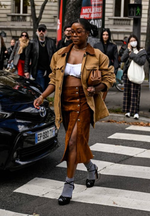 Guest is seen wearing a brown Miu Miu jacket, white bustier, brown Miu Miu skirt, beige Miu Miu bag and black shoes with gray socks outside the Miu...