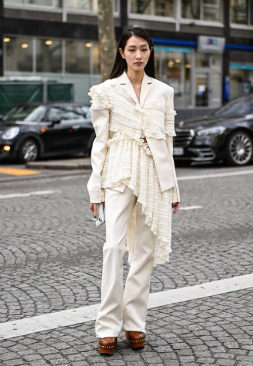 Guest is seen wearing a cream Rokh ruffled top, white Rokh pants and brown shoes outside the Rokh show during the Womenswear Fall/Winter 2025/2026 as...