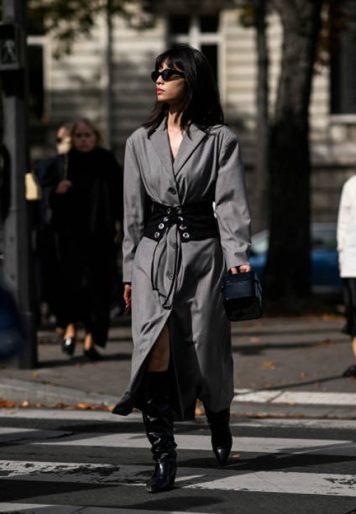 Guest is seen wearing a gray trench coat, black and silver belt, black boots and black sunglasses outside the Miu Miu show during the Womenswear...