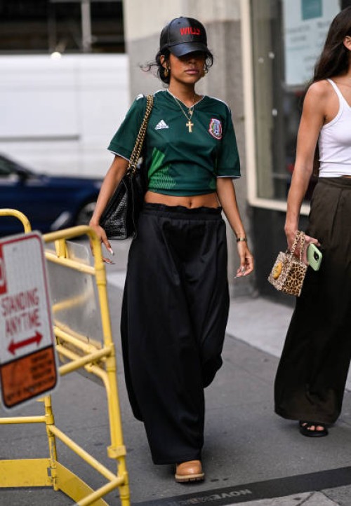 Guest is seen wearing a green Adidas collab t-shirt, Willy Chavarria black and red hat, black pants with a black and gold chain bag outside the Willy...