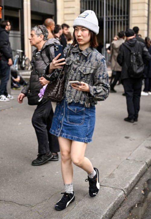 Guest is seen wearing a Sacai jacket, denim skirt, black sneakers and gray beanie outside the Sacai show during Womenswear Spring/Summer 2025 as part...