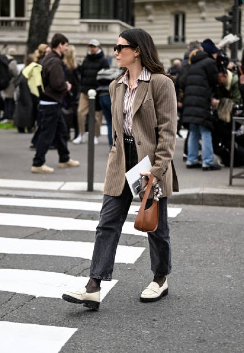 Guest is seen wearing a tan striped jacket, stripe shirt, gray pants and cream shoes with brown bag outside the Miu Miu show during the Womenswear...